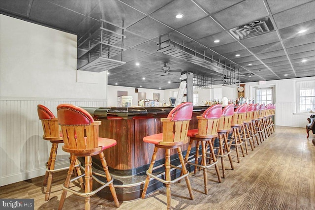 bar with a paneled ceiling, ceiling fan, and light hardwood / wood-style flooring