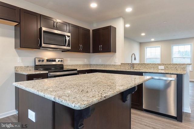 kitchen with stainless steel appliances, sink, light stone countertops, and light wood-type flooring