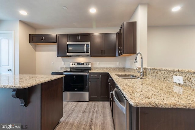 kitchen featuring dark brown cabinetry, light stone counters, stainless steel appliances, light wood-type flooring, and sink