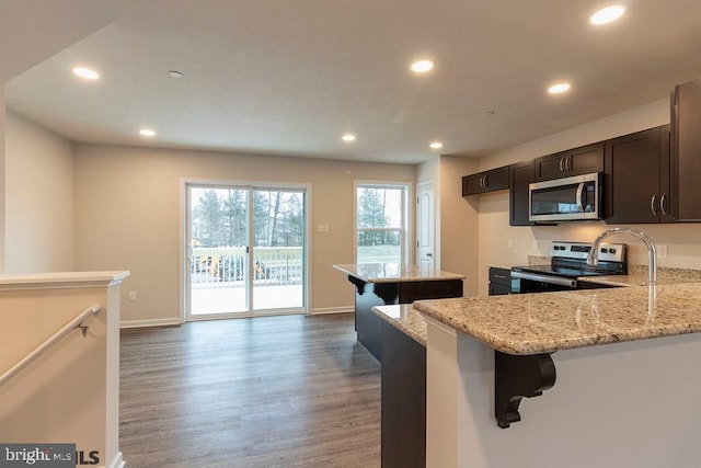 kitchen with kitchen peninsula, stainless steel appliances, light stone countertops, wood-type flooring, and a breakfast bar