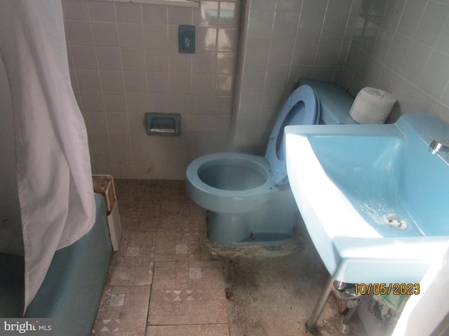 bathroom with toilet, tile floors, sink, and tile walls