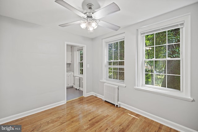 empty room featuring ceiling fan, light wood-type flooring, and radiator