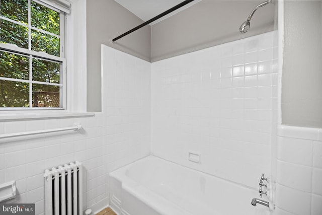 bathroom featuring tile walls, tiled shower / bath, and radiator heating unit