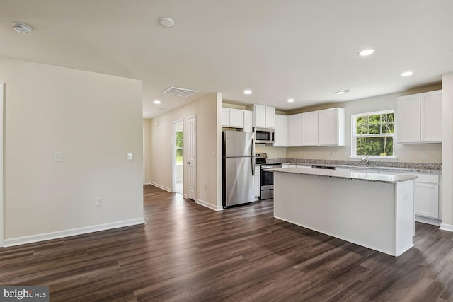 kitchen featuring white cabinetry, appliances with stainless steel finishes, light stone countertops, and a kitchen island