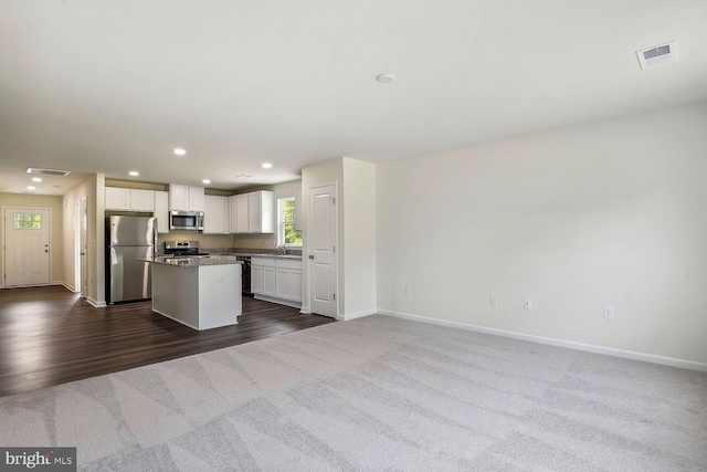 kitchen featuring stainless steel appliances, dark colored carpet, a kitchen island, and white cabinets