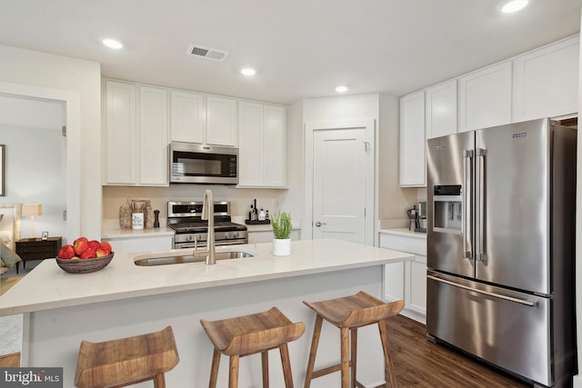 kitchen featuring dark wood-type flooring, sink, white cabinetry, a center island with sink, and appliances with stainless steel finishes