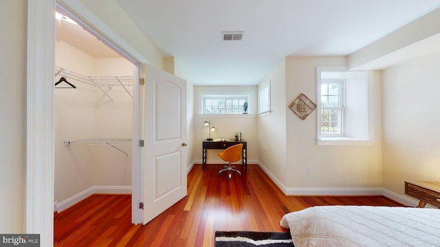 bedroom with a spacious closet, a closet, multiple windows, and dark hardwood / wood-style floors