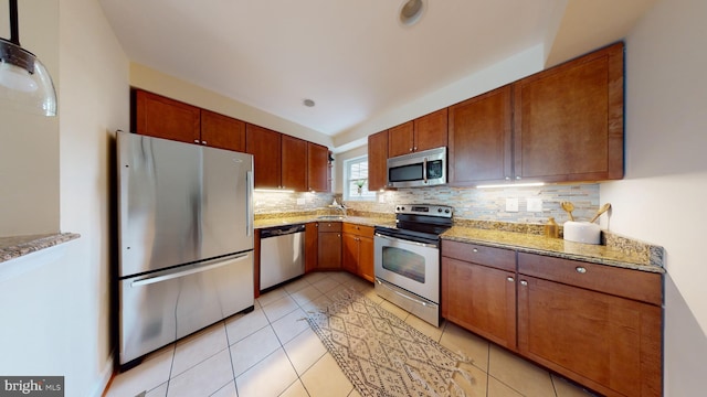 kitchen featuring appliances with stainless steel finishes, tasteful backsplash, light stone counters, and light tile floors