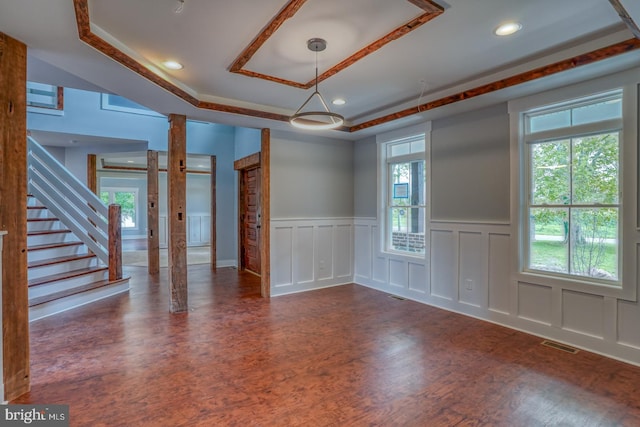 empty room with a healthy amount of sunlight, a tray ceiling, and ornate columns