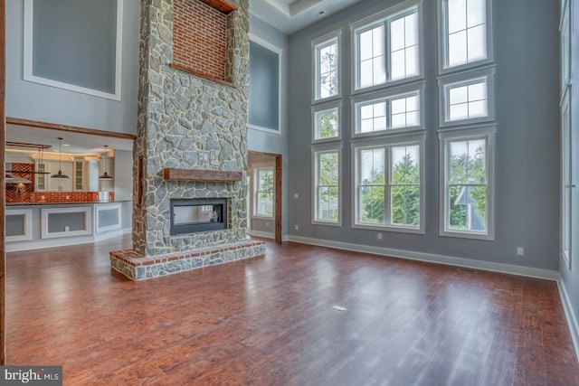 unfurnished living room featuring a stone fireplace, plenty of natural light, a high ceiling, and dark wood-type flooring