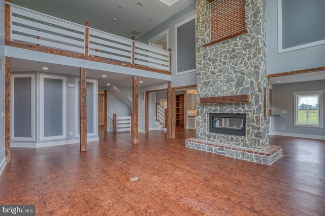 unfurnished living room with a high ceiling, dark wood-type flooring, decorative columns, and a fireplace