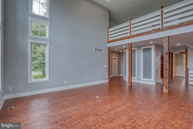 unfurnished living room featuring dark hardwood / wood-style floors, a healthy amount of sunlight, and a towering ceiling