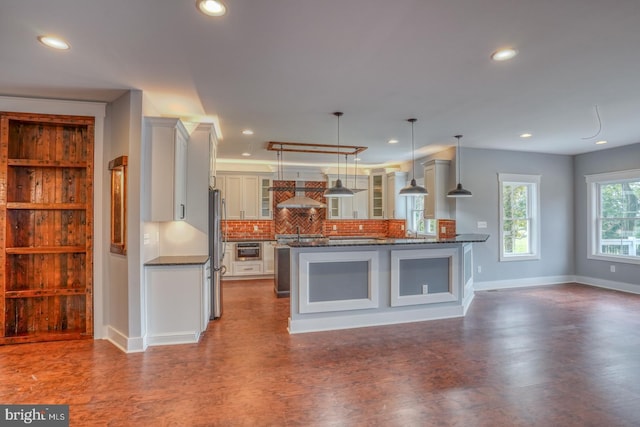 kitchen featuring white cabinets, backsplash, stainless steel appliances, wall chimney range hood, and decorative light fixtures