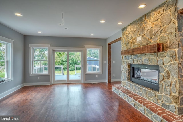 unfurnished living room with a fireplace, dark wood-type flooring, and a wealth of natural light