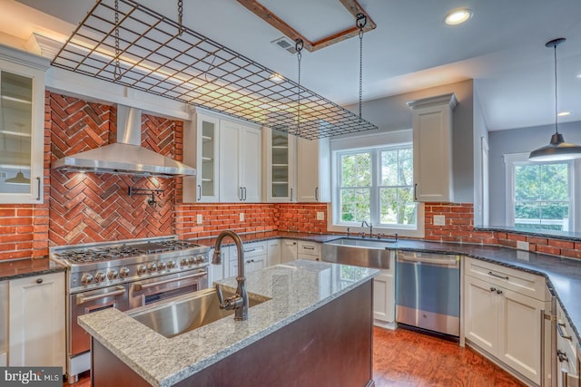 kitchen with dark stone countertops, white cabinets, stainless steel appliances, and wall chimney range hood