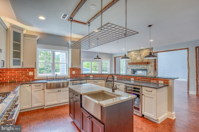 kitchen featuring an island with sink, wood-type flooring, sink, and a stone fireplace