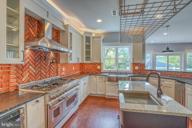 kitchen featuring backsplash, dark stone countertops, double oven range, wall chimney exhaust hood, and pendant lighting