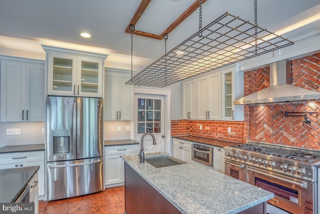 kitchen with appliances with stainless steel finishes, dark stone countertops, pendant lighting, wall chimney exhaust hood, and sink