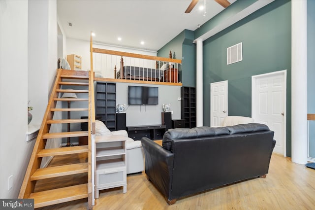 living room featuring light hardwood / wood-style floors, ceiling fan, and a towering ceiling