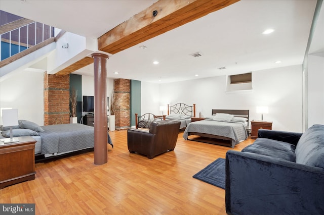 bedroom with beam ceiling, brick wall, ornate columns, and light hardwood / wood-style flooring