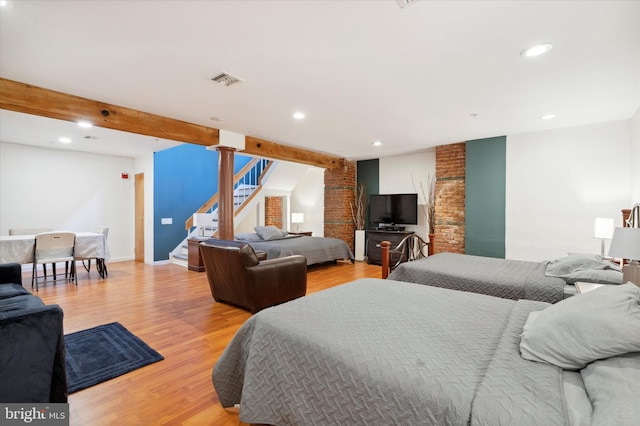 bedroom featuring beam ceiling, brick wall, ornate columns, and light wood-type flooring