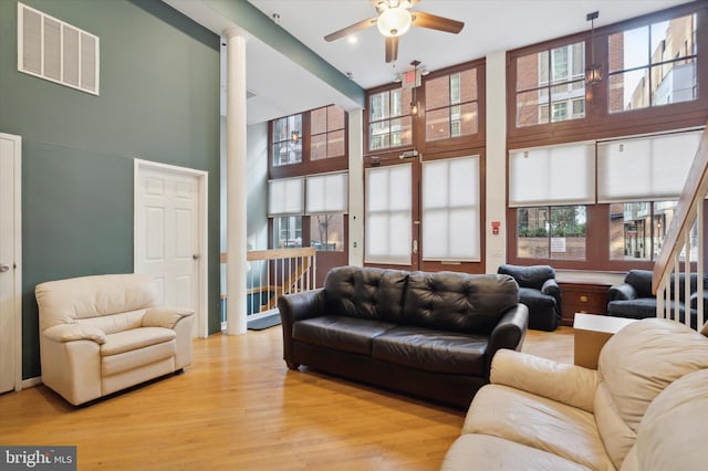 living room with ceiling fan, a high ceiling, light hardwood / wood-style floors, and a healthy amount of sunlight