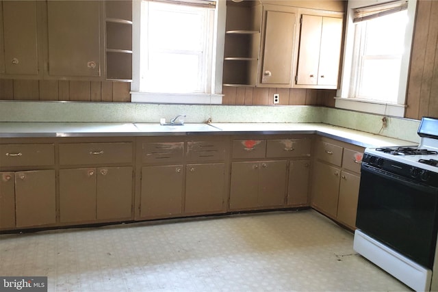 kitchen with light tile floors, white gas range oven, and sink