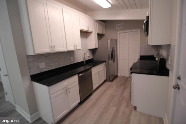 kitchen with appliances with stainless steel finishes, vaulted ceiling, white cabinets, and light hardwood / wood-style flooring