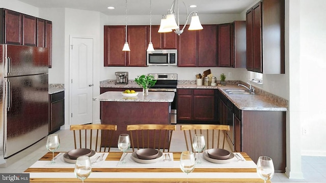 kitchen featuring sink, a center island, appliances with stainless steel finishes, pendant lighting, and light stone countertops