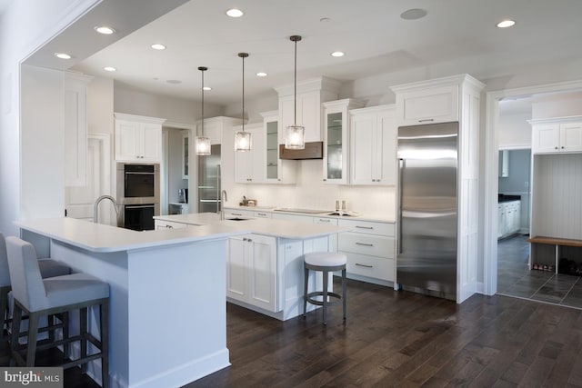 kitchen featuring white cabinets, pendant lighting, range hood, dark hardwood / wood-style floors, and appliances with stainless steel finishes