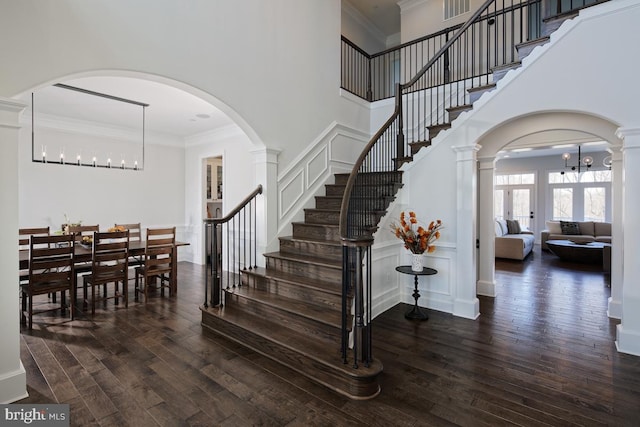 stairs featuring ornamental molding, decorative columns, dark hardwood / wood-style floors, and a high ceiling