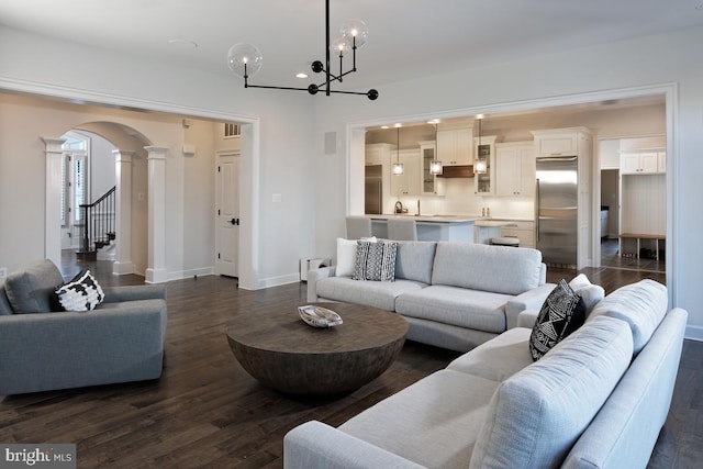 living room with decorative columns, dark wood-type flooring, and a chandelier