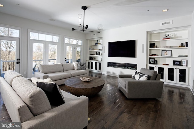 living room featuring built in features, dark hardwood / wood-style flooring, an inviting chandelier, and french doors