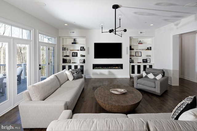 living room featuring dark wood-type flooring, built in shelves, and an inviting chandelier