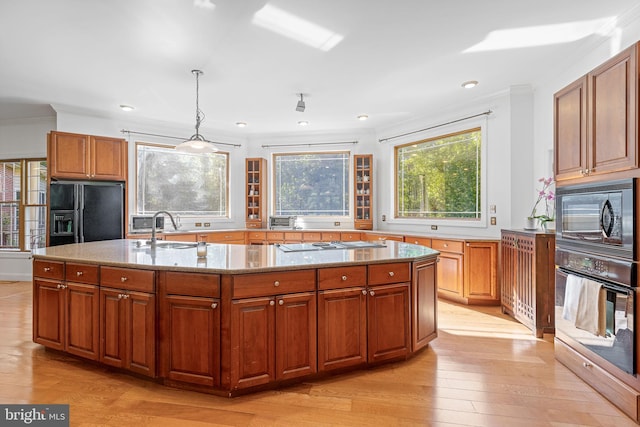 kitchen featuring light stone countertops, hanging light fixtures, crown molding, black appliances, and light wood-type flooring