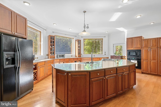 kitchen with a kitchen island with sink, sink, black appliances, pendant lighting, and light hardwood / wood-style flooring