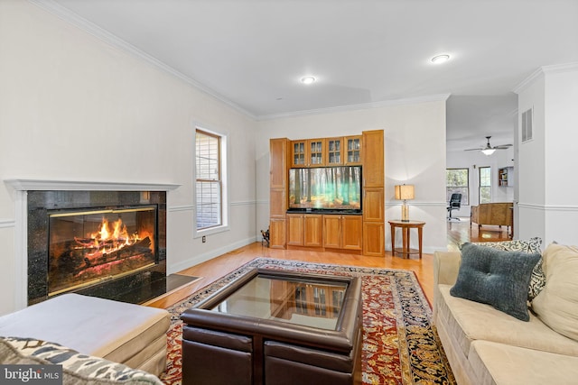 living room featuring light wood-type flooring, ceiling fan, crown molding, and a premium fireplace