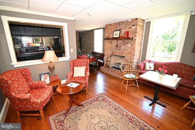 living room with a paneled ceiling, brick wall, dark hardwood / wood-style floors, and a brick fireplace