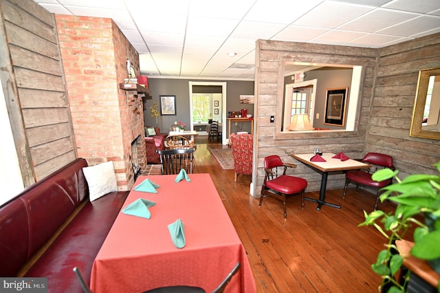 dining area featuring dark hardwood / wood-style flooring, a brick fireplace, a drop ceiling, and wooden walls