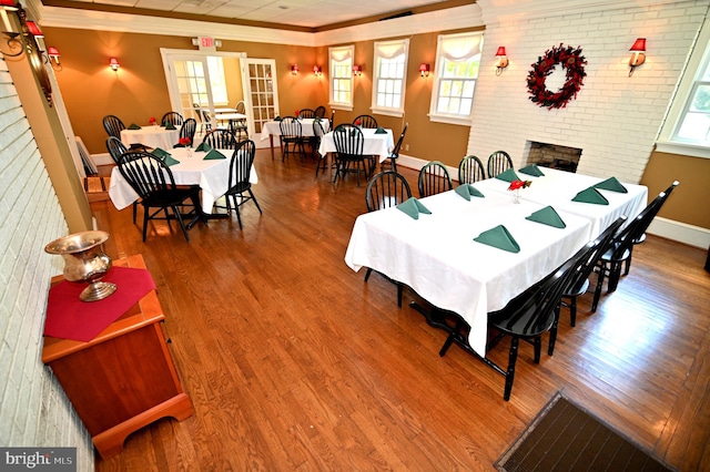 dining space with crown molding, a brick fireplace, wood-type flooring, and a wealth of natural light