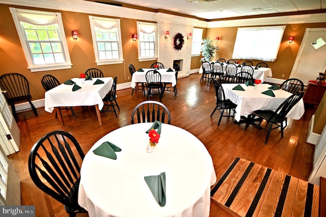 dining room with a fireplace, brick wall, ornamental molding, and hardwood / wood-style floors