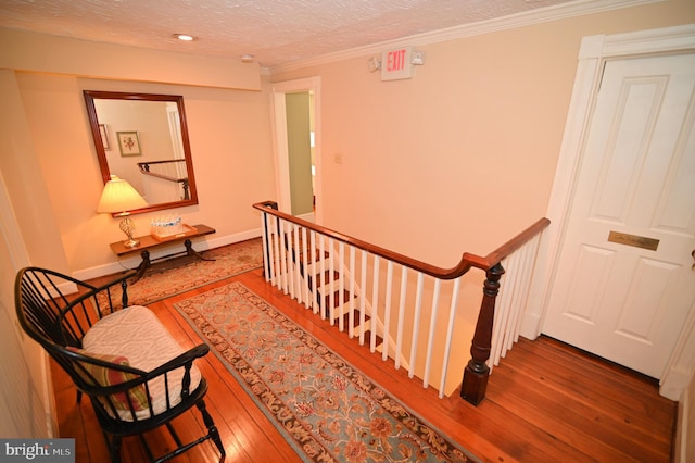 stairway with a textured ceiling, wood-type flooring, and ornamental molding