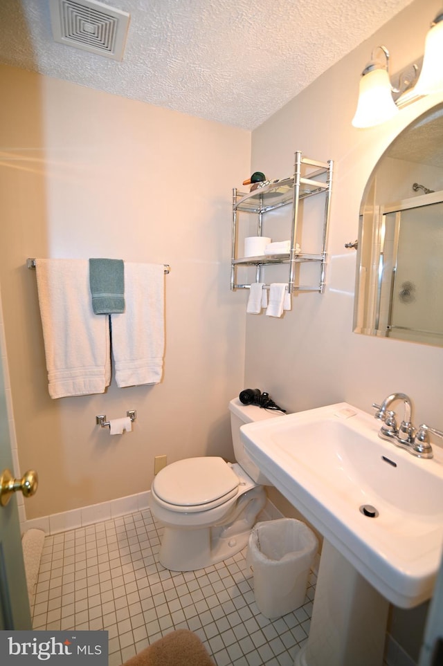 bathroom with a textured ceiling, toilet, tile floors, and sink