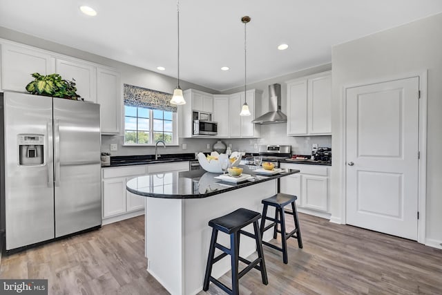 kitchen with wall chimney exhaust hood, a kitchen island, stainless steel appliances, and light hardwood / wood-style flooring