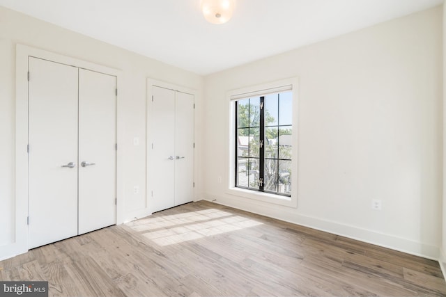 unfurnished bedroom with multiple closets and light hardwood / wood-style flooring