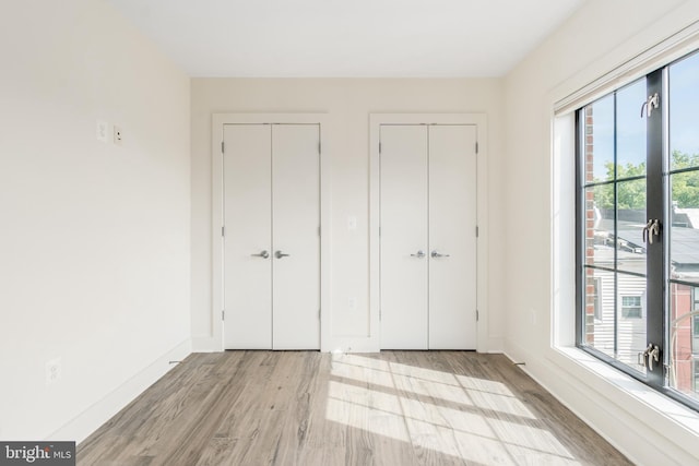 unfurnished bedroom featuring light hardwood / wood-style flooring, multiple closets, and multiple windows