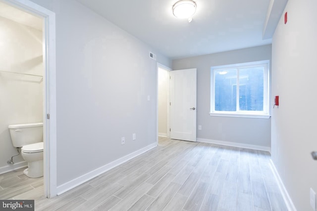 unfurnished bedroom featuring ensuite bathroom and light hardwood / wood-style flooring