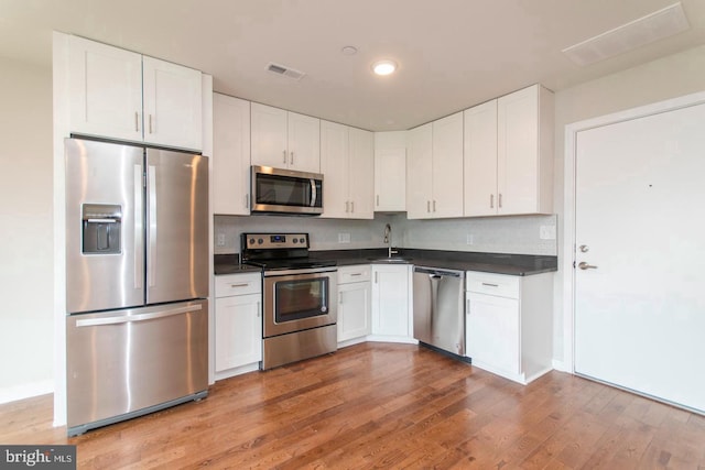 kitchen featuring stainless steel appliances, white cabinets, backsplash, light wood-type flooring, and sink