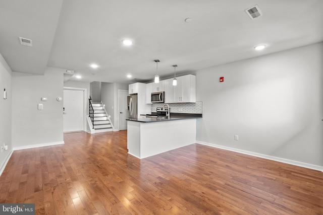 kitchen with stainless steel appliances, decorative light fixtures, hardwood / wood-style flooring, kitchen peninsula, and backsplash