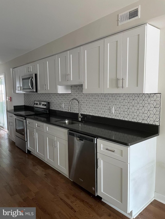 kitchen featuring appliances with stainless steel finishes, white cabinets, backsplash, dark hardwood / wood-style floors, and sink